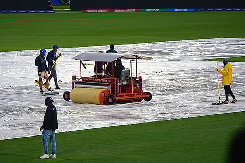 Groundsmen clear water from the covers